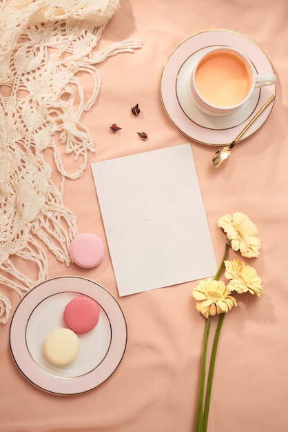 Foto envelope, flores e macarons com uma xícara de chá sobre fundo claro