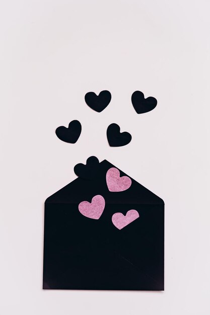 envelope preto com corações de papel preto e rosa em um fundo claro preparação para Valentines D