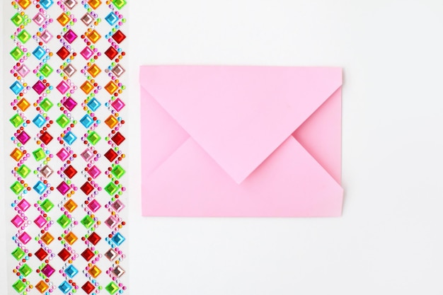 Envelope rosa e um conjunto de strass multicoloridos para decoração em fundo branco Fazendo cartão postal em envelope para o dia dos namorados faça você mesmo Foto da série