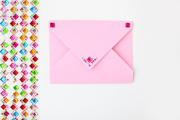 Envelope rosa e um conjunto de strass multicoloridos para decoração em fundo branco Fazendo cartão postal em envelope para o dia dos namorados faça você mesmo Foto da série