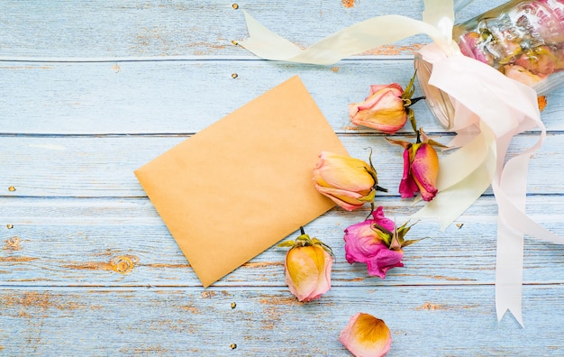 Envelope vazio em um fundo de madeira, rodeado por flores rosas