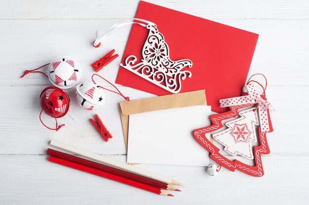 Envelope vermelho em branco, nota vazia e brinquedos de Natal brancos em madeira rústica, plana leigos