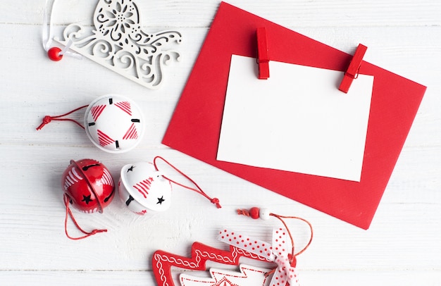 Envelope vermelho em branco, nota vazia e brinquedos de Natal brancos em madeira rústica, plana leigos