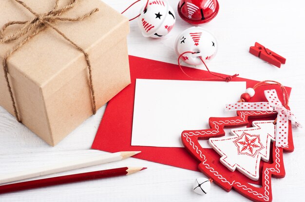 Envelope vermelho em branco, nota vazia e brinquedos de Natal brancos em madeira rústica