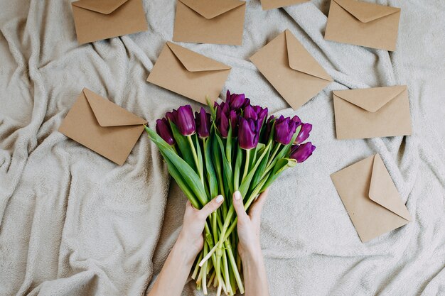 Envelopes de papel ofício em xadrez bege, flores da primavera, monte de tulipas roxas com envelopes, mulher detém monte de tulipas roxas.