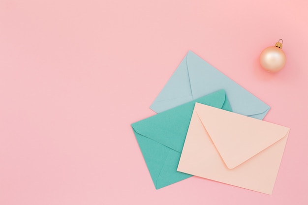 Envelopes postais coloridos e bola de natal em fundo rosa, copie o espaço.