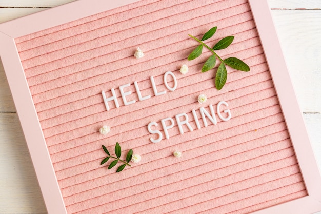 Envíe un mensaje de texto Hola primavera en el pizarrón rosa con ramas verdes y flores de gypsophila sobre fondo de madera, composición de estilo minimalista, copie el espacio para su texto.