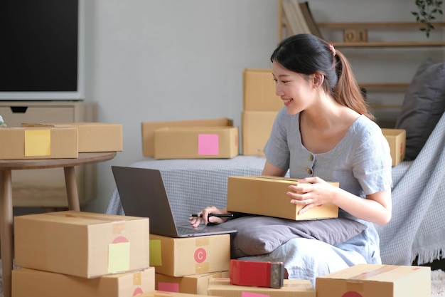 Envío de compras en línea joven propietario de una pequeña empresa que comienza a escribir una dirección en una caja de cartón en el lugar de trabajoempresario de pequeñas empresas PYME o mujer asiática independiente que trabaja con una caja en casa