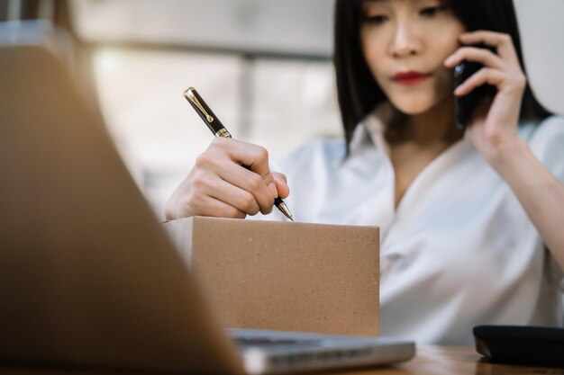 Envío de compras en línea mujer puesta en marcha propietario de una pequeña empresa escribiendo la dirección en una caja de cartón en el lugar de trabajoemprendedor de pequeñas empresas PYME o mujer asiática independiente que trabaja con una caja en casa