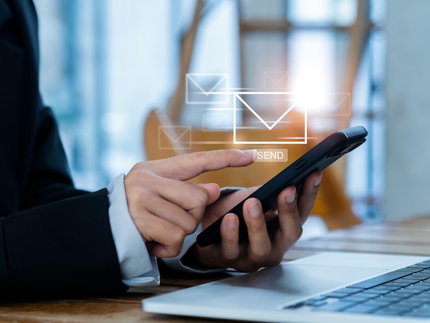 Envío de correo electrónico y conceptos de marketing empresarial Movimiento rápido del icono de letras digitales que aparece mientras una persona de negocios que usa un teléfono inteligente móvil y una computadora portátil en el lugar de trabajo envía un mensaje