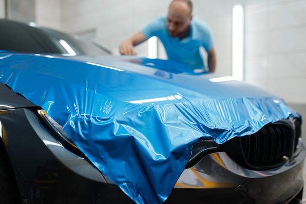 Envoltura de automóviles, el hombre instala una lámina protectora de vinilo o una película en el capó. Trabajador hace detalles automáticos