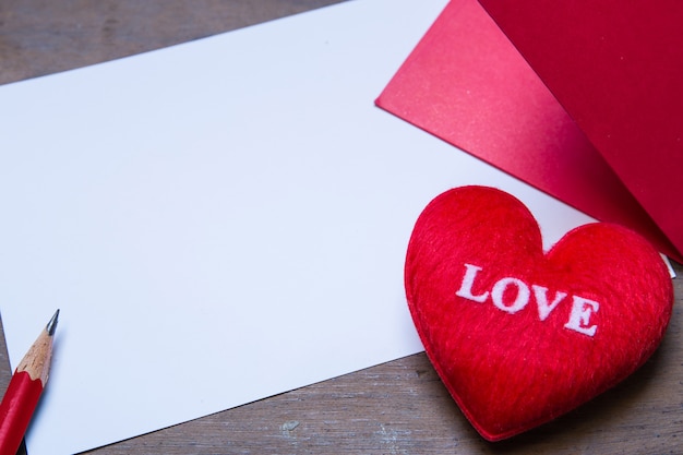 envolvente roja con almohada de corazón de forma sobre amor de texto, hoja de papel y sobre fondo de madera