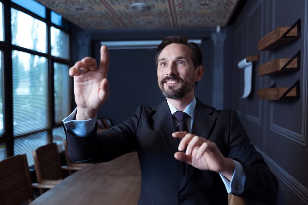 Envolvido na atividade. Homem feliz, positivo e confiante em frente a um painel sensorial virtual e pressionando a mão na tela enquanto trabalha na realidade virtual