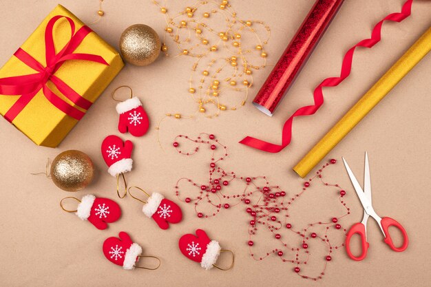 Envolviendo regalos de Navidad. Papel de regalo brillante, rojo y dorado, tijeras, cuentas, bolas navideñas y pequeñas manoplas decorativas ubicadas en color beige. . Vacaciones.