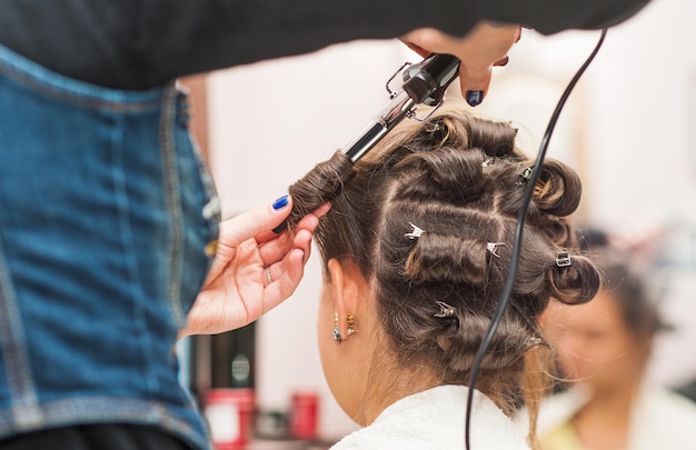 Envuelva el peluquero que se encrespa plancha que se encrespa Mujer del salón de belleza hace el peinado del pelo