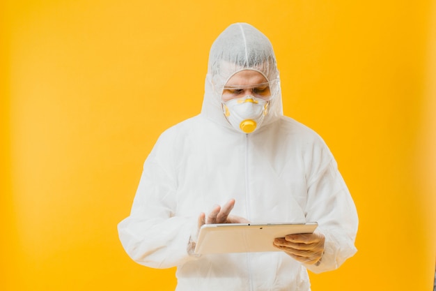 Foto epidemiologe im hazmatanzug und in der atemschutzmaske, die digitale tablette auf gelber wand halten