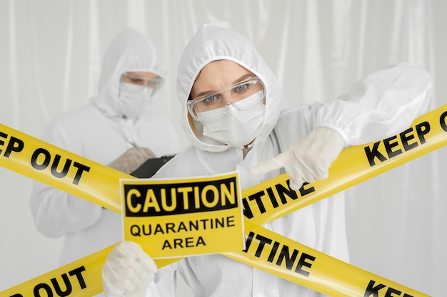 Epidemiologen, ein Mann und eine Frau in Schutzkleidung, befinden sich in einem Sperrgebiet mit einem Warnschild