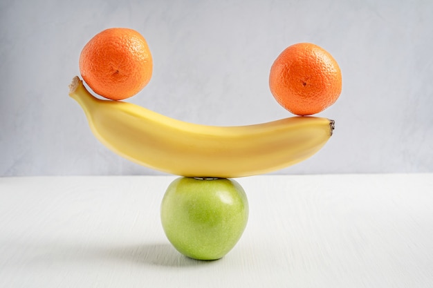 Equilibrar ou equilibrar tangerina crua, banana madura e maçã azeda verde na mesa de madeira branca