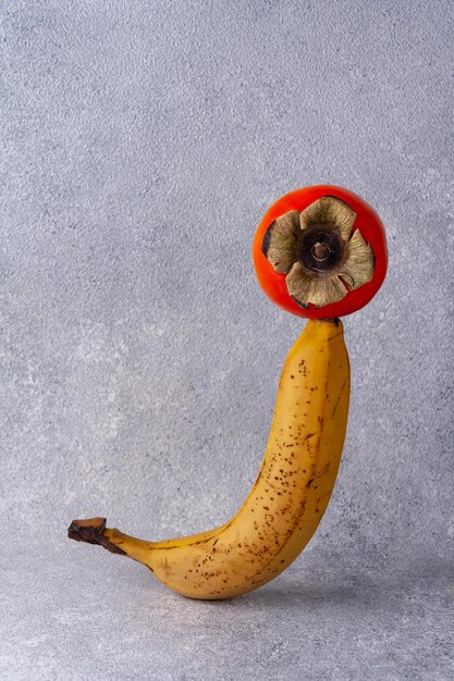 Foto equilibre banana madura e caqui em fundo cinza, lugar para texto