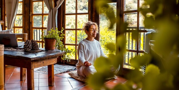 Foto equilíbrio interior e amor por si mesmo conceito de estilo de vida uma mulher jovem de meia-idade fazendo meditação na posição de yoga asana em casa sentada no chão exercício natural saudável bem-estar mental