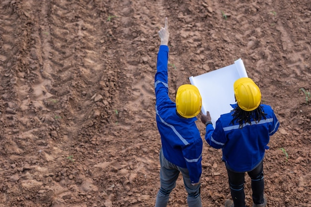 Equipa de agrimensores de terra trabalhando juntos na construção consulte o estudo de campo procurando a localização do edifício com a planta