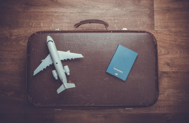 Equipaje antiguo, figurilla de avión, pasaporte sobre piso de madera