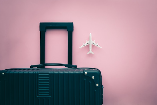 Equipaje negro y modelo de avión blanco sobre fondo rosa para el concepto de viaje y viaje