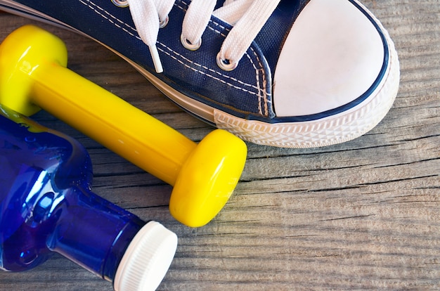 Foto equipamento de fitness. garrafa de água azul, haltere amarelo e sapatilha em fundo de madeira. conceito de estilo de vida saudável, esporte ou fitness.