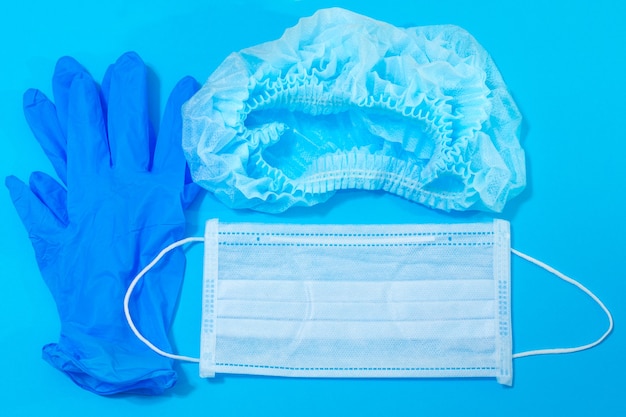 Equipamento de proteção individual - máscara médica, chapéu, luvas de borracha em um fundo azul, proteção médica contra vírus
