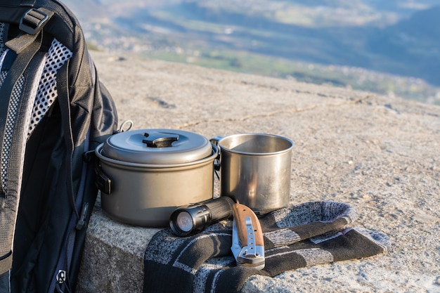 Equipamento de rastreio ou caminhada definido na cerca de concreto. Mochila, meias, copo de metal, chaleira, faca dobrável e lanterna. Conceito de atividade ao ar livre.