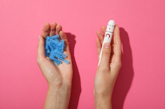 Equipamento médico para diabéticos em mãos na vista superior de fundo rosa