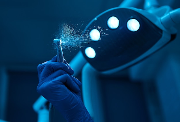 Foto equipamento profissional utilizado em odontologia. close-up da mão de dentista cirurgião segurando a broca dentária com salpicos de água no fundo de uma luz de lâmpada médica incluída. copie o espaço. prática dental