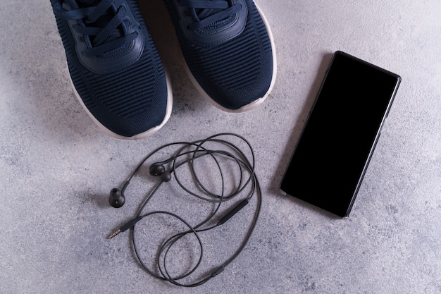 Equipamentos de ginástica com tênis, smartphone e fones de ouvido cinza