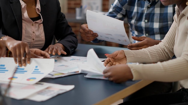 Equipe afro-americana de pessoas fazendo trabalho em equipe para planejar a análise de projetos no escritório, examinando documentos com estatísticas e relatórios. Colegas colaborando na pesquisa. Fechar-se. Tiro de mão.