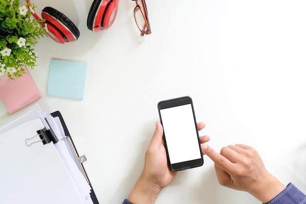 Equipe as mãos usando a zombaria acima da exposição vazia do smartphone móvel no espaço de trabalho da vista superior.