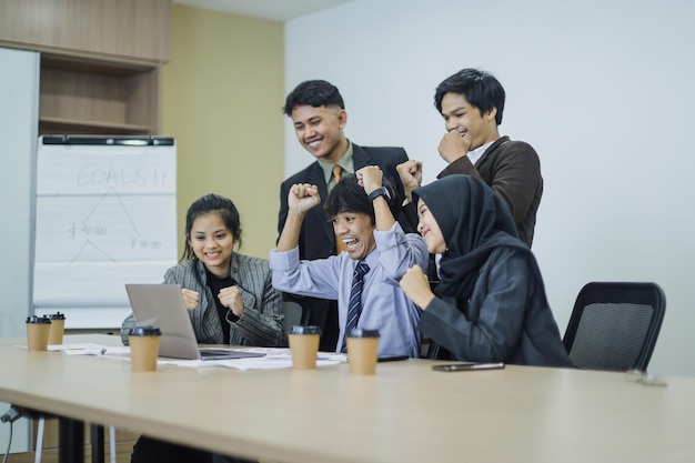 Equipe bem-sucedida de colegas de trabalho está olhando para o laptop e celebra a vitória juntos na reunião