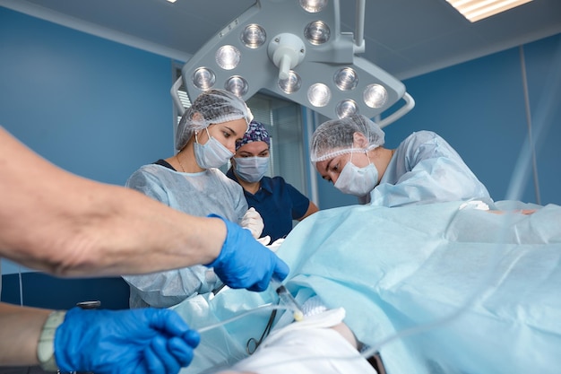 Equipe cirúrgica concentrada operando um paciente em uma sala de operações Anestesiologista bem treinado com anos de treinamento com máquinas complexas acompanha o paciente durante toda a cirurgia
