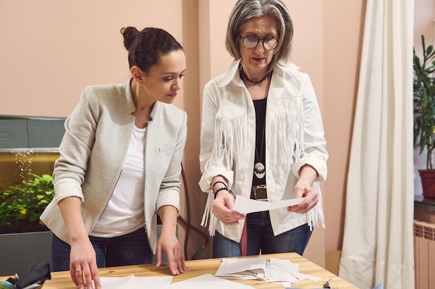 Equipe criativa e qualificada de duas mulheres designers de moda costureiras que visualizam esboços de moda e discutem padrões de costura enquanto trabalham no ateliê de design de roupas