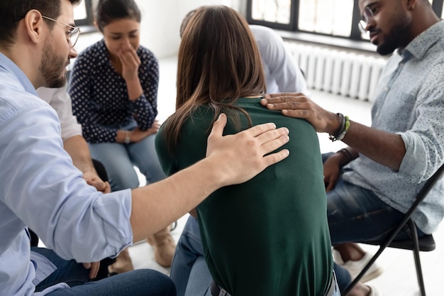 Equipe de apoio consolando um companheiro de grupo infeliz e choroso em uma reunião em um centro de saúde mental de assistência Amigos de reabilitação diversos tocando o ombro dando ajuda e conforto a uma menina chateada contando uma história de vida triste
