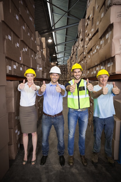 Equipe de armazém sorrindo na câmera mostrando polegares para cima