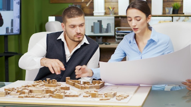 Equipe de arquiteto segurando a planta e trabalhando com modelos de construção para o projeto de nova cidade.