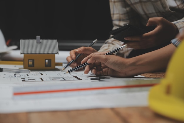 Equipe de arquitetos multiétnicos trabalhando em planos de construção na sala de reuniões Engenheiros discutindo sobre projeto no escritório Empresário maduro e mulher em pé ao redor da mesa trabalhando na planta