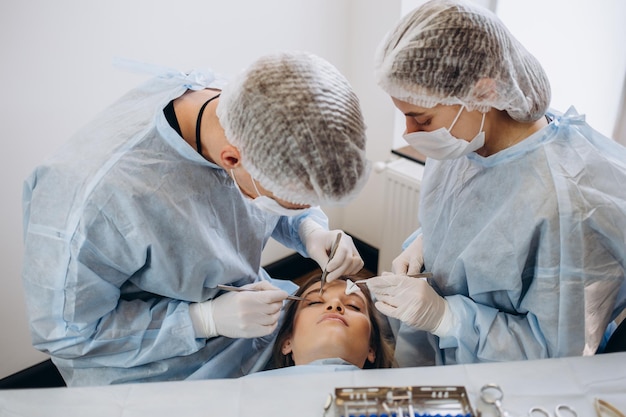 Equipe de cirurgião de uniforme realiza operação em um paciente na clínica de cirurgia plástica