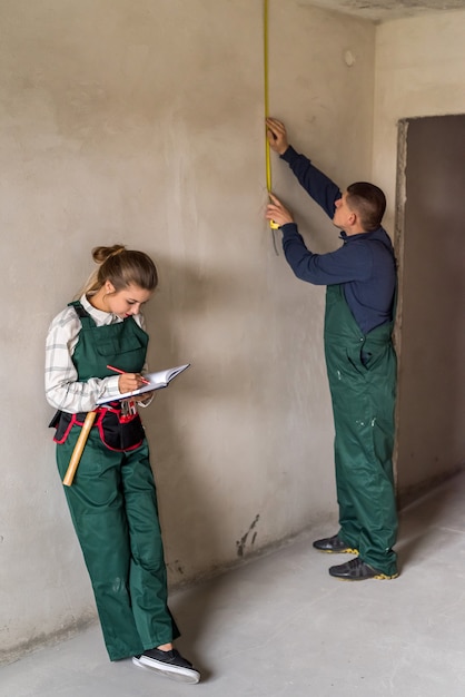 Equipe de construtores medindo paredes e escrevendo no bloco de notas