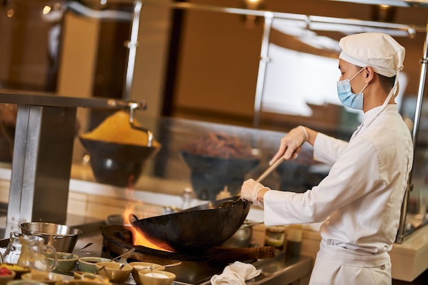 Equipe de cozinha concentrada usando máscara e cozinhando na wok