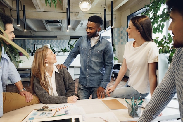 Equipe de diversos colegas de trabalho em um escritório moderno discute seu projeto juntos