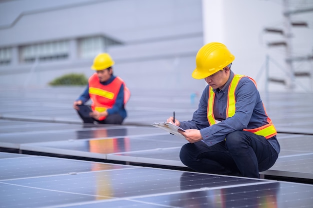 Equipe de engenheiros asiáticos inspecionando a qualidade do sistema de energia de células solares de energia solar no telhado da fábrica