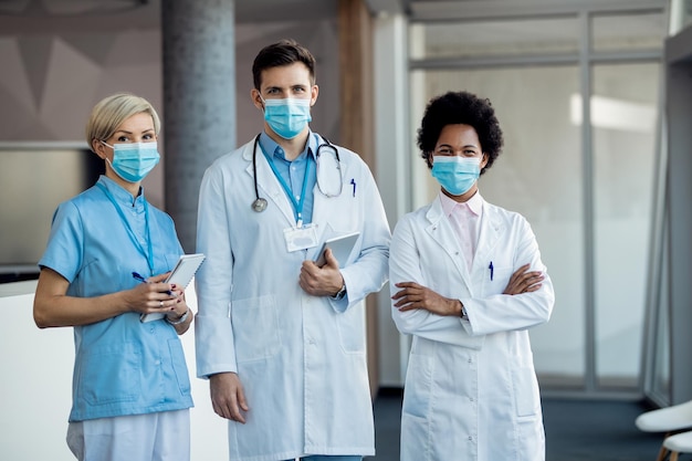 Equipe de especialistas médicos confiantes com máscaras protetoras em um corredor do hospital