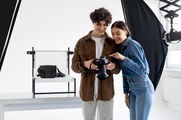 Equipe de fotógrafo profissional e assistente feminina verificando fotos na câmera fotográfica enquanto faz sessão de fotos de conteúdo