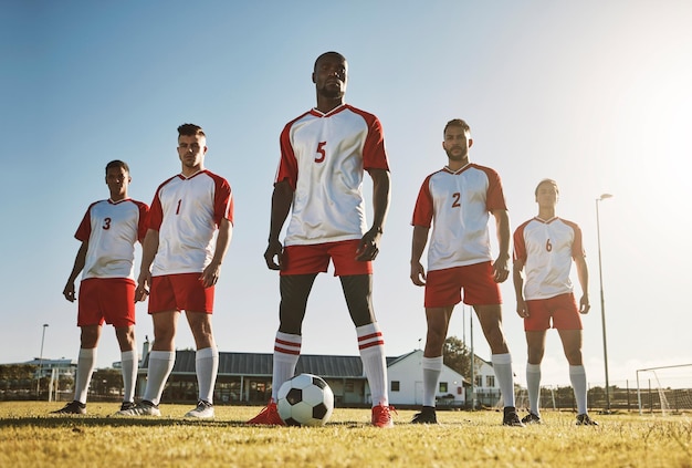 Equipe de jogadores de futebol e treinamento esportivo no campo de futebol por homens em pé com poder de bola e mentalidade forte Aptidão de futebol e jogadores de futebol masculinos unidos em apoio no campo de futebol para treino